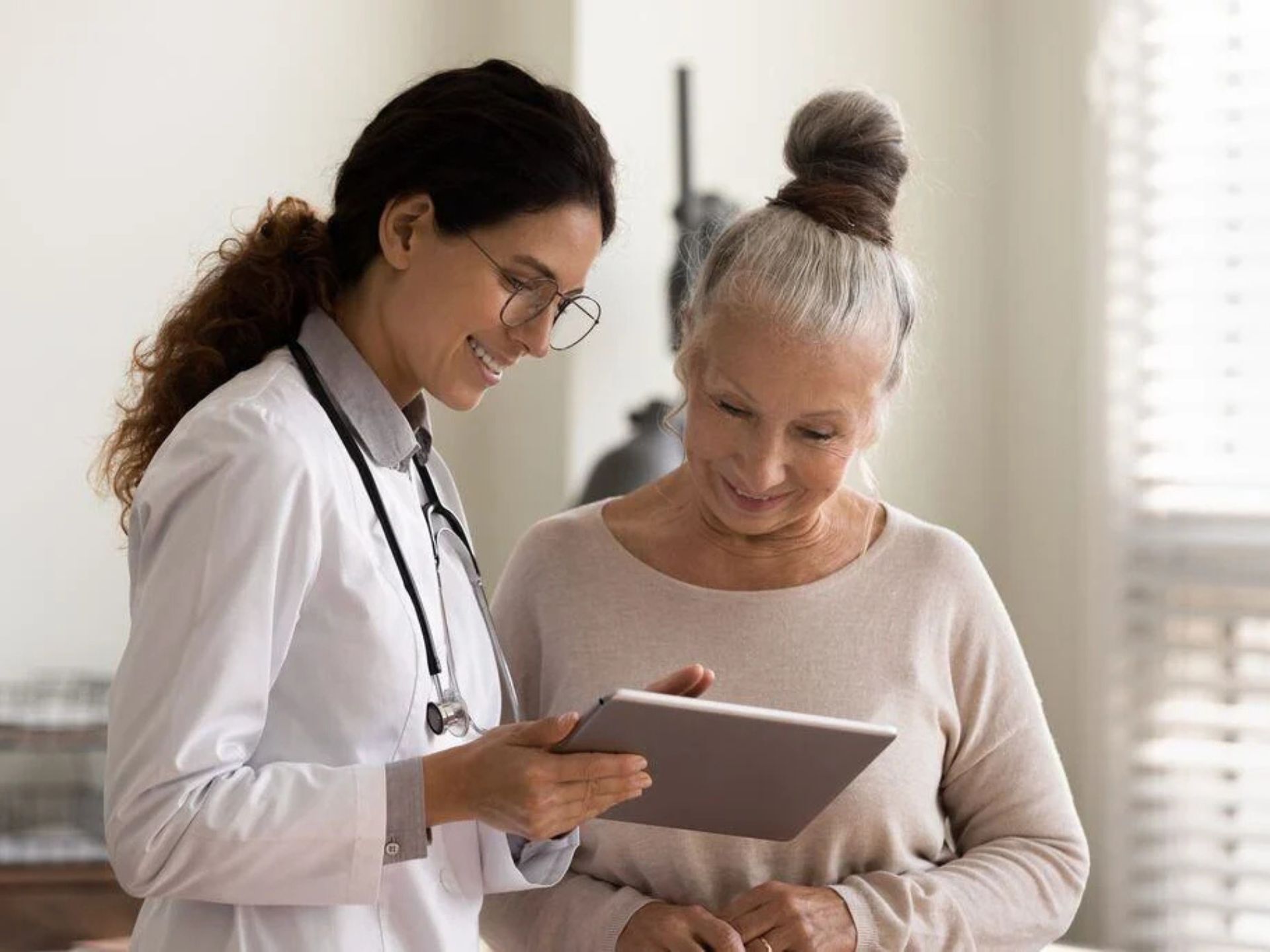 A healthcare professional in a lab coat discusses medical information with an elderly woman, both engaged and attentive.