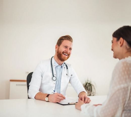 A man and woman converse with a doctor at a table in a medical consultation setting.