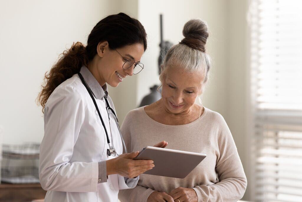 Happy female doctor and senior patient look at tablet