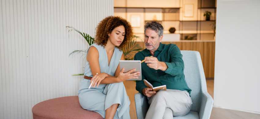 A woman and a man engaged in a discussion while reviewing a tablet, seated in a modern, stylish office space.
