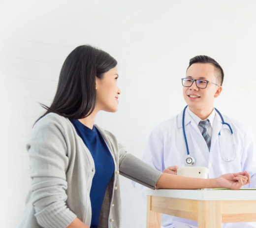 A doctor speaks to a seated woman, discussing her health in a clinical setting