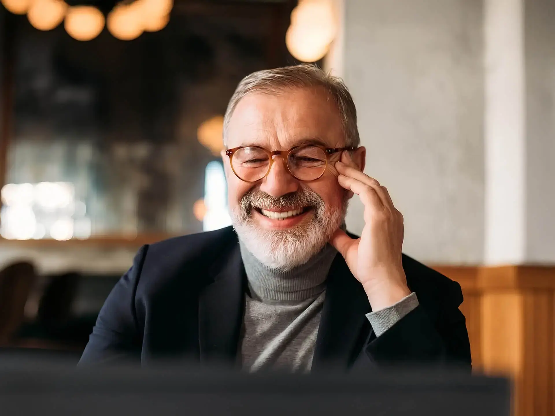 Older man with glasses and beard smiling while looking at computer screen